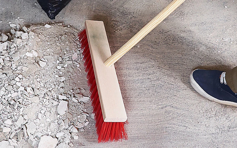 Reinigungsarbeiten auf der Baustelle: Schutt und Staub werden mit einem Besen zusammengefegt
