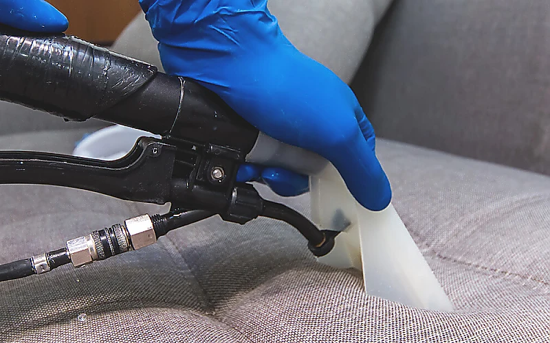 Professionelle Polsterreinigung: Verschmutzungen werden mit einem Reinigungsgerät aus dem Sofa entfernt